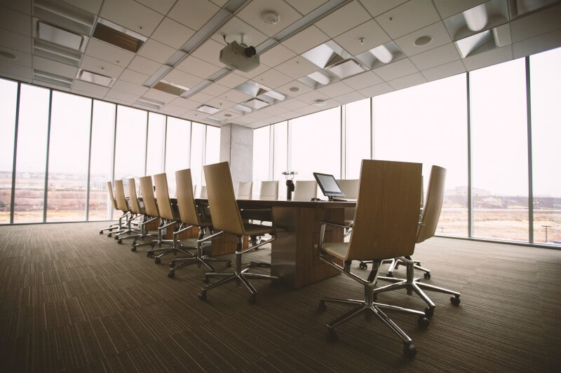 A long meeting-room table lined with high-backed chairs beside floor-to-ceiling windows.